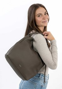 Sac à dos en cuir brun avec une surface texturée et une forme arrondie. Dispose de bretelles ajustables et d'une fermeture éclair sur le dessus pour un accès facile.