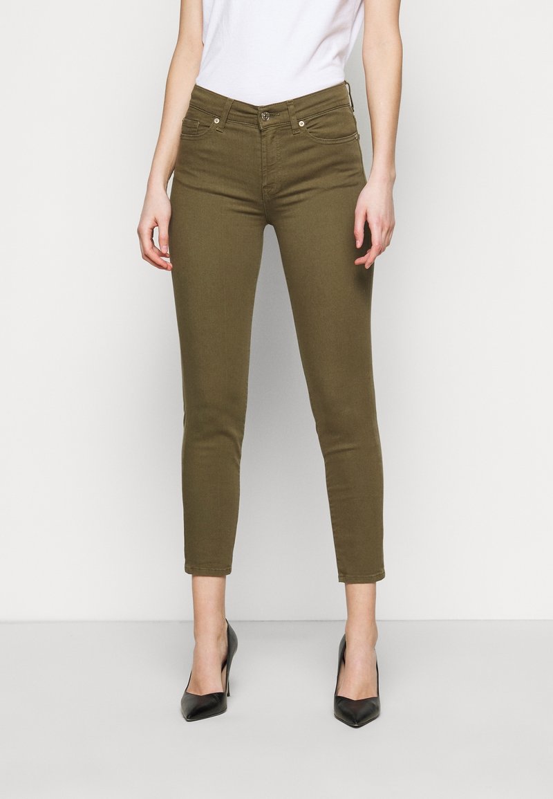 Jeans ajustados de color verde oliva con cintura media, piernas ajustadas y costuras de contraste, combinados con zapatos de tacón negros.