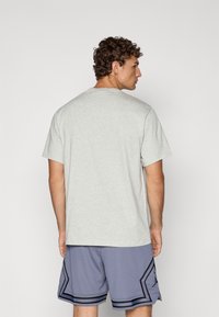 Camiseta de manga corta gris claro con cuello redondo, combinada con pantalones cortos deportivos de malla azules con acentos negros y un diseño geométrico.