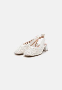 Chaussures à talons slingback blanches en dentelle avec un bout pointu, ornées de motifs floraux, d'un petit talon carré et d'un accent en nœud à l'arrière pour plus de détail.