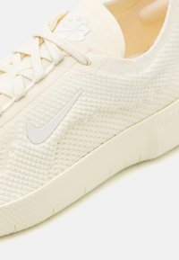 Białe, teksturowane sneakersy z plecionym wzorem, z białym logo Nike i dopasowanymi sznurówkami, osadzone na kremowej gumowej podeszwie.