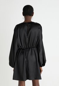 Melna satīna kleita ar garām, uzpūstām piedurknēm, elastīgu jostasvietu un aizmugurē slēgtu pogu. Gluda tekstūra ar vienkāršu, elegantu dizainu.