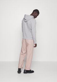 Gray hoodie with a large hood, paired with light pink trousers, and black shoes. The hoodie has ribbed cuffs and a casual fit.