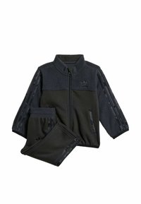 Černý sportovní teplákový komplet s fleecovou horní částí, zipovou bundou a odpovídajícími kalhotami s pruhovanými detaily na rukávech a po stranách.