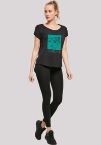 Sort t-shirt med et turkist grafisk design, der viser hænder, parret med sorte leggings og sorte sportssko. Casual, afslappet pasform.