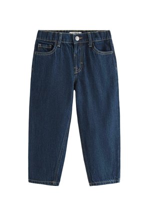 Smilende ung dreng står med den ene hånd i siden iført en enkel hvid T-shirt, mørkeblå jeans og hvide sneakers mod en ensfarvet baggrund.
