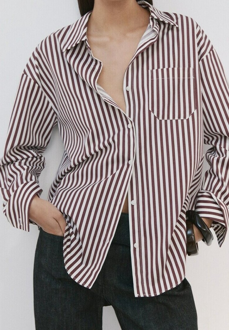 Personne portant une chemise ample à rayures verticales bordeaux et blanches, une main dans la poche et un bracelet noir au poignet.