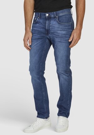 Denim jeans in dark blue, regular fit. Features five pockets, a button fly, and subtle fading. Paired with white sneakers.