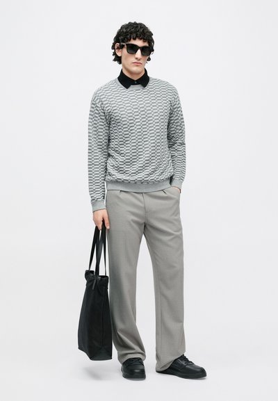 Suéter cinzento com padrão, camisa preta com colarinho por baixo, calças cinzentas, sapatilhas pretas e uma mala tote preta. A modelo usa óculos de sol escuros.