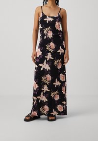 Robe longue fleurie en tissu noir, ornée de fleurs rose pâle et violettes. Conçue avec des bretelles fines ajustables et une silhouette simple.