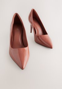 Ružičaste lakirane cipele s visokim potpeticama, šiljastim vrhom i tankom štiklom. Glatka završna obrada i podstavljeni unutrašnjost.