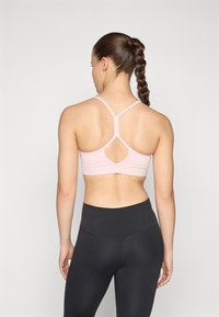 Sutiã de desporto rosa com tiras cruzadas nas costas e detalhe recortado, combinado com leggings pretas de cintura alta, textura suave, design ajustado.