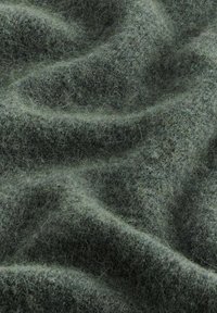 Tissu en laine vert avec une surface douce et texturée, présentant des variations subtiles de teinte et de densité, créant une apparence ondulée.