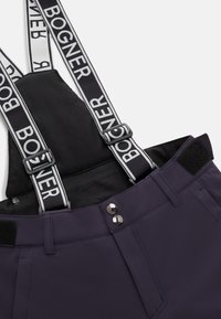 Fialové lyžařské kalhoty s černým předním dílem a nastavitelnými popruhy, které mají bílé logo "BOGNER". Kovové knoflíky a suchý zip v pase. Hladká tkanina.