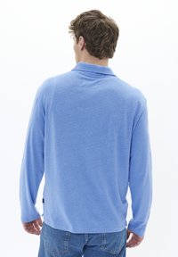 Long-sleeve polo shirt in light blue, made of soft fabric, featuring a classic collar and a curved hem, with a small logo at the hem.