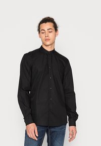 Camicia nera button-up con colletto alto, realizzata in tessuto morbido, con maniche lunghe e design aderente. Finitura con bottoni neri.