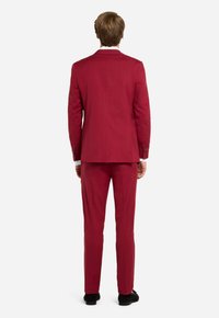 Completo rosso con pantaloni abbinati, caratterizzato da una vestibilità strutturata, tessuto liscio e hardware discreto sulle maniche. Design della schiena semplice.