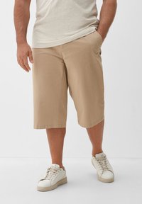 Beige katoenen shorts met zakken, knielengte en een ontspannen pasvorm. Gecombineerd met witte sneakers voor een casual uitstraling.