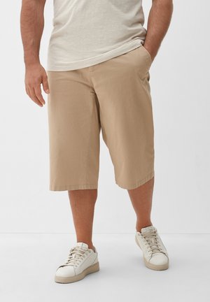 Shorts en coton beige avec poches, de longueur genou et coupe décontractée. Associés à des baskets blanches pour un look décontracté.