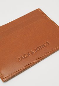 Tarjetero de cuero marrón con bordes cosidos, que cuenta con múltiples ranuras para tarjetas y el nombre de la marca "JACK & JONES" en relieve en la superficie.
