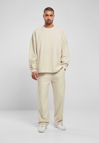 Beanie en joggingset, ribbeltextuur, lichtbeige kleur, relaxte pasvorm, lange mouwen, bijpassende broek met een rechte snit en zijzakken.