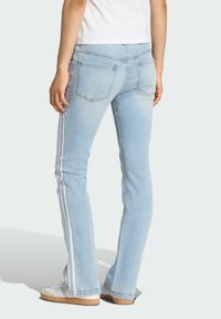 Svetlomodré džínsy s rozšíreným strihom, s bielymi bočnými prúžkami a zadnými vreckami. Nosia sa s bielymi teniskami.