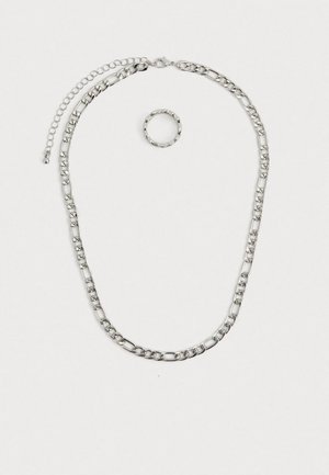 Hõbedatooniline ehetesett, mis sisaldab paksu kettkaelakeed lukuga ja sellele sobivat tekstuuriga sõrmust. Mõlemad osad on läikivad ja metallilised.