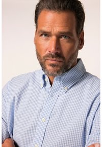 Camisa de cuadros azul y blanca con cuello, que presenta una tela texturizada. La camisa tiene un corte relajado y botones visibles.