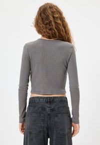Grå kortærmet top i ribbet materiale med rund halsudskæring. Sammen med højhalsede sorte jeans, som viser designet bagpå.