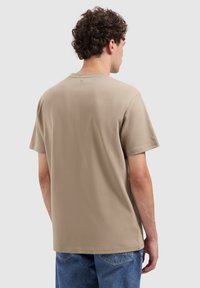 Beige katoenen t-shirt met korte mouwen en een ronde hals. Heeft een vlakke achterkant met een subtiele logodetail nabij de halslijn.