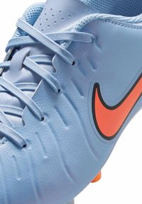 Hellblauer Fußballschuh mit strukturierter synthetischer Oberseite, orangefarbenem Nike-Swoosh, dünnen Schnürsenkeln und mehreren Traktionsstollen an der Sohle.