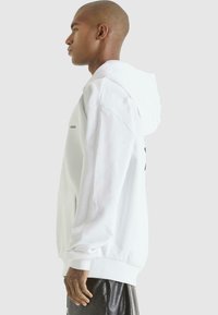 White hooded sweatshirt with a front pocket, ribbed cuffs, and hem. Features subtle branding on the chest and a smooth texture.