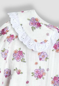 Tessuto a fiori con colletto in pizzo bianco a occhielli. Presenta fiori rosa, viola e arancioni su uno sfondo bianco. Morbido al tatto.