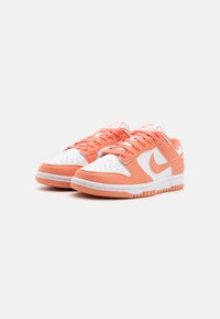 Nike Dunk-sneakers har en hvit lær tåboks, oransje semsket overlegg, og en gummisåle. Snøring og merkevare er også oransje.