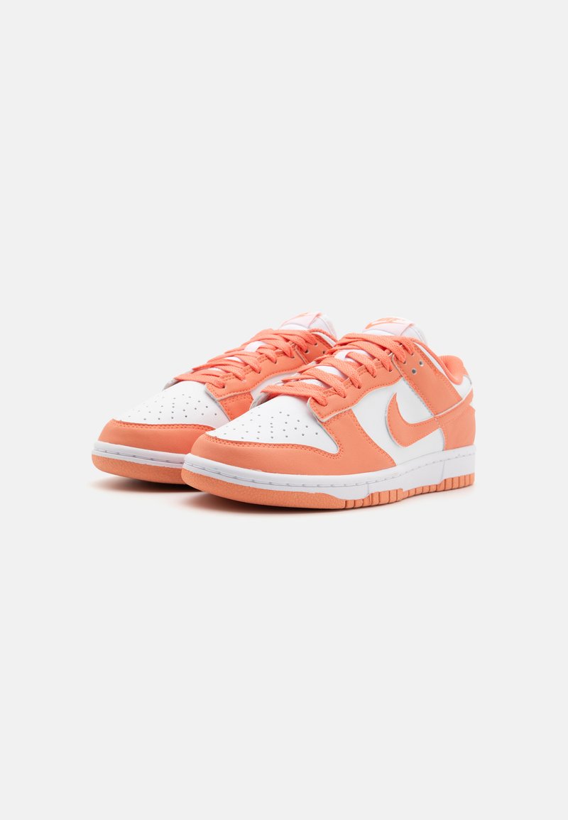 Les baskets Nike Dunk présentent une boîte à orteils en cuir blanc, des superpositions en daim orange et une semelle en caoutchouc. Les lacets et la marque sont également orange.