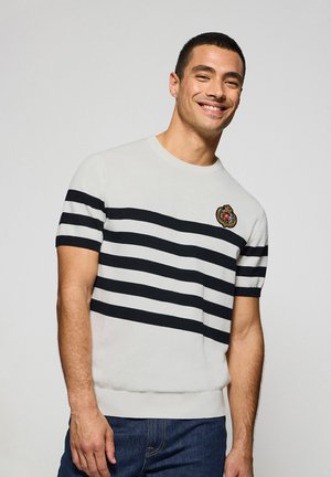 Weißer Kurzarmpullover mit schwarzen horizontalen Streifen, geripptem Hals- und Saumabschluss, versehen mit einem gestickten Emblem auf der Brust.
