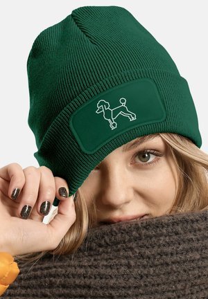 Green knitted beanie featuring a rectangular patch with a white outline of a dog. Soft texture with ribbed design.