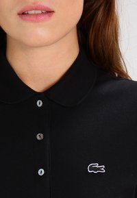 Polo shirt nero con una vestibilità slim. Presenta un colletto appuntito e tre bottoni. Il iconico logo del coccodrillo Lacoste è ricamato in bianco.
