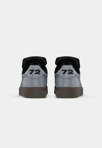 Et par grå sneakers med sorte kraver og brune såler, hver viser tallet 72 på hælen mot en hvit bakgrunn.