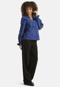 Blue floral-embroidered blouse with a v-neck and ruffled cuffs, paired with black wide-leg pants and black shoes. Smooth texture.