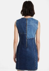Abito in denim senza maniche, caratterizzato da un motivo a blocchi di colore blu chiaro e scuro, con una zip sul retro e dettagli con orlo sfrangiato.