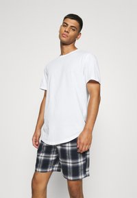 Weißes T-Shirt mit kurzen Ärmeln und abgerundetem Saum, kombiniert mit karierten Shorts in Marineblau und Weiß, die eine weiche Textur und einen lässigen Schnitt bieten.