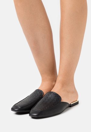 Black leather mules with a woven texture on the upper, pointed toe, and a small, square heel. Smooth finish, minimalist design.