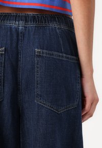 Dark blue denim pants with an elastic waistband and two back pockets, featuring yellow stitching and a soft texture.