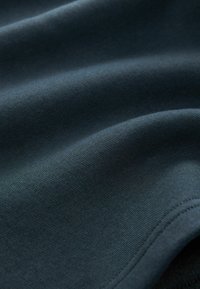 Tela de algodón azul oscuro con una textura suave, que presenta suaves curvas y pliegues. Los bordes están terminados con un sutil detalle de costura.