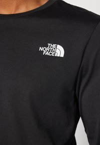 Černé bavlněné tričko s bílým logem "The North Face" na levé části hrudi. Design s kulatým výstřihem a hladkou texturou.
