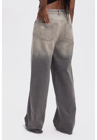 Jeans de pierna ancha en gris claro con un degradado que oscurece hacia el fondo. Presenta dos bolsillos traseros con detalle de logotipo en relieve.