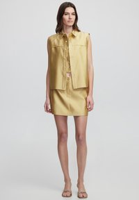 Gold sleeveless shirt jacket with buttons and a straight-fit mini skirt. Smooth fabric, clean lines, and a minimalist design.