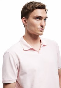 Jasnoróżowa koszulka polo o teksturowanej tkaninie, z krótkimi rękawami i klasycznym kołnierzykiem. Posiada subtelne wykończenie kontrastowe w kołnierzu.