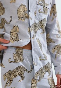 Conjunto de camisa abotonada y pantalones cortos con tela a rayas azul y blanca que presenta un patrón repetido de estampado de leopardo. Textura suave, diseño casual.